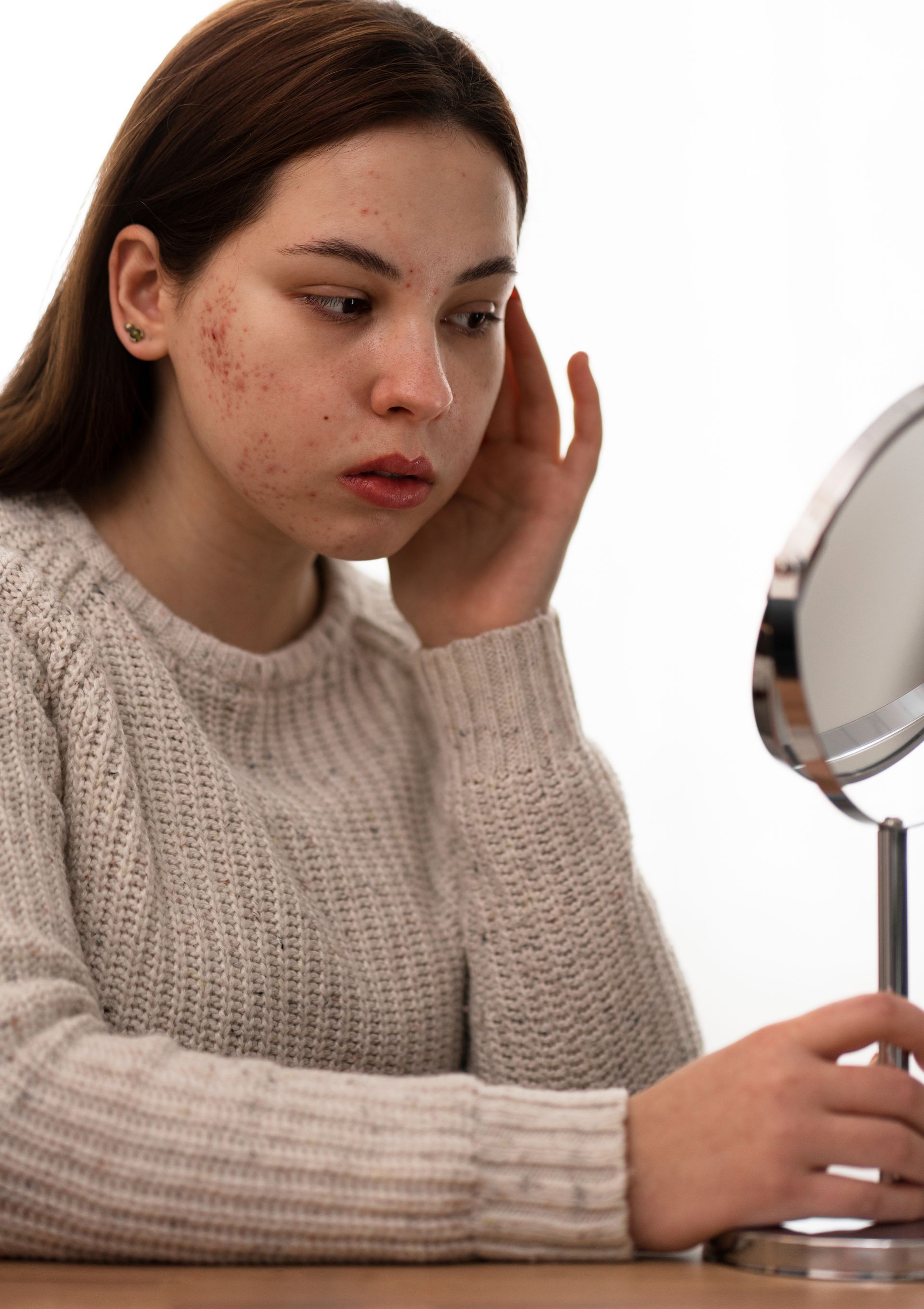 A woman is looking at her face in a mirror.