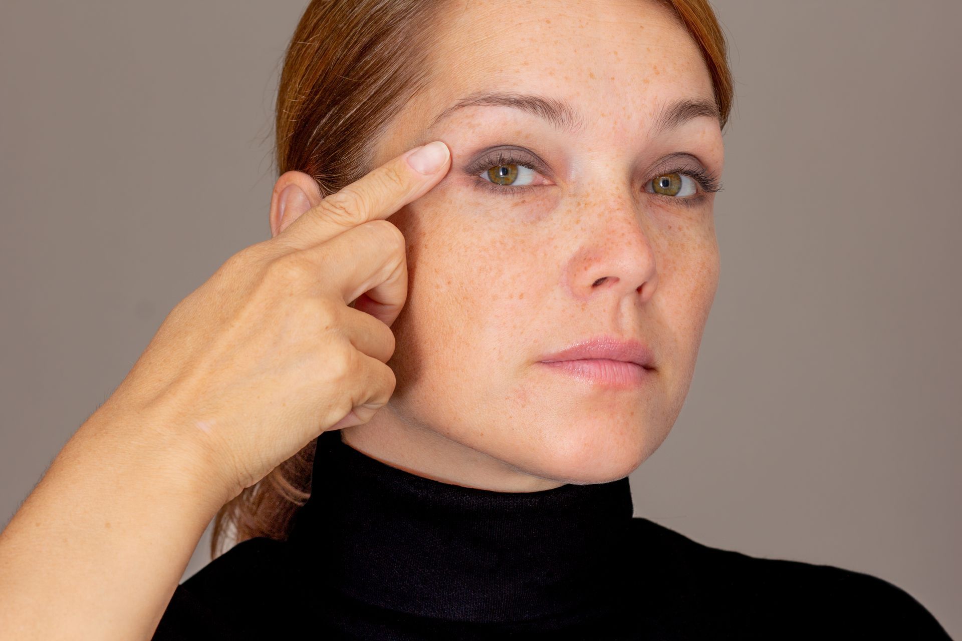 A woman is pointing at her eye with her finger.