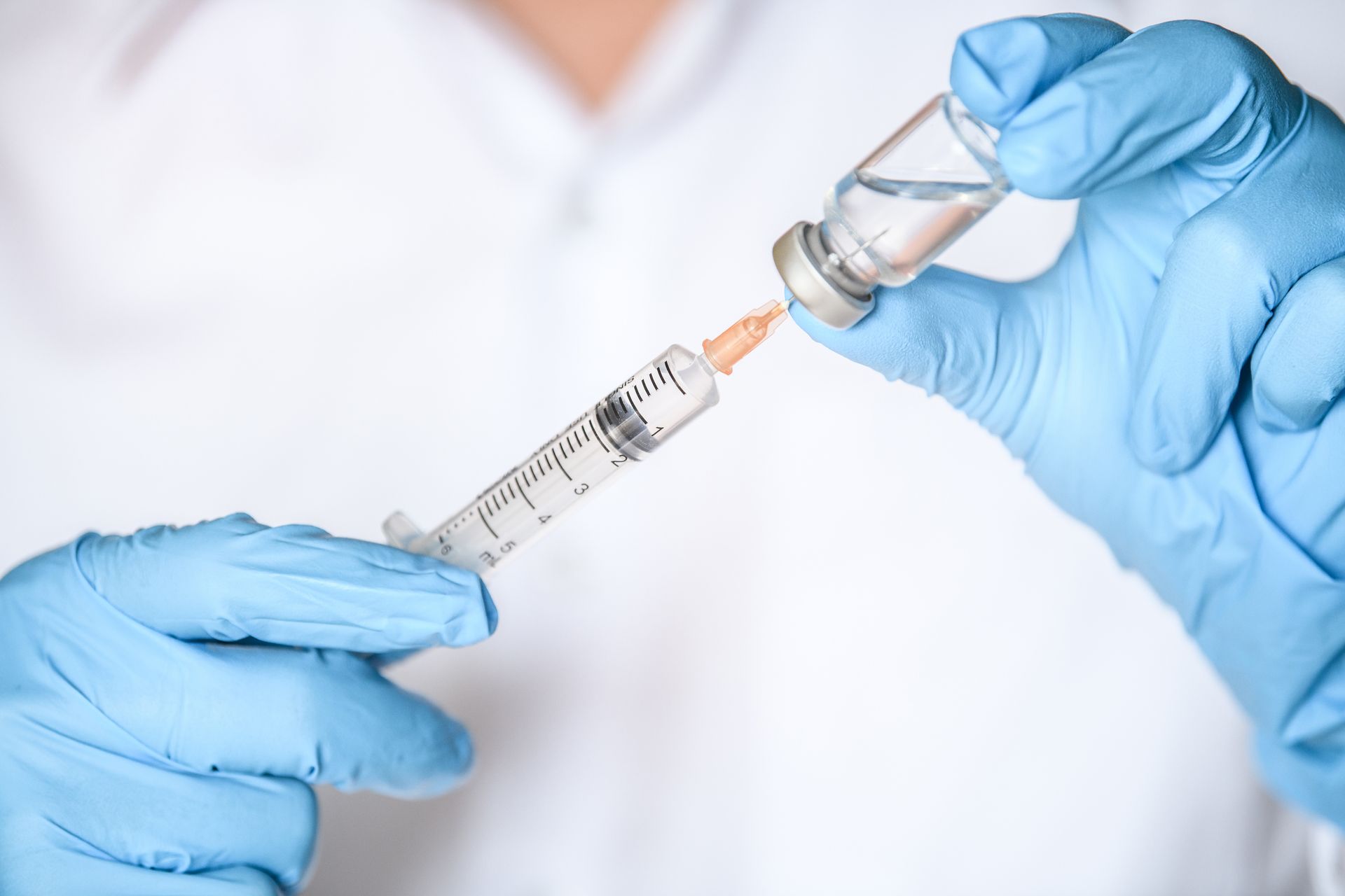 Person in blue gloves filling a syringe with liquid from a vial, medical setting.