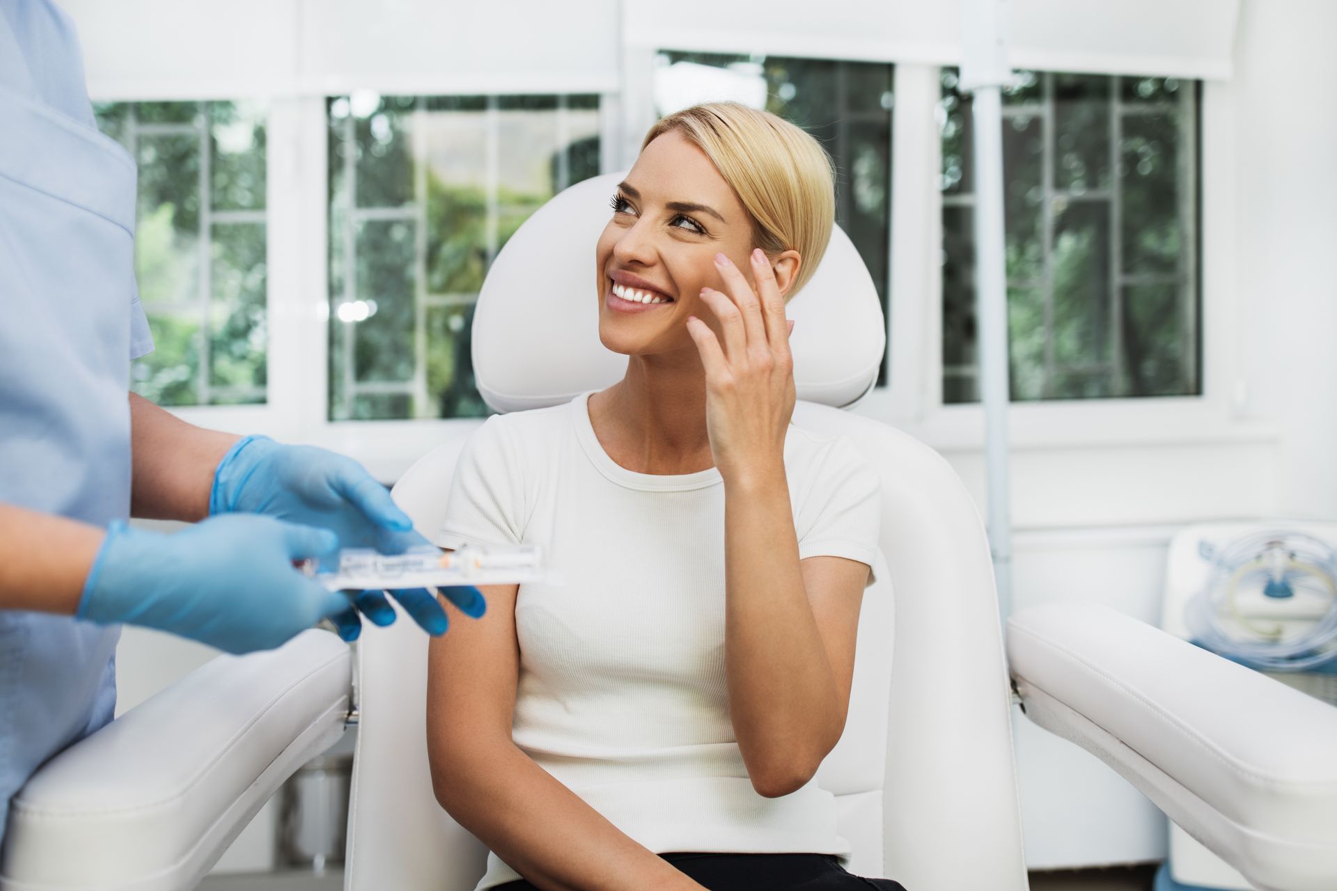 Woman smiles in a medical chair as someone holds a tray of medical supplies in a clinic.