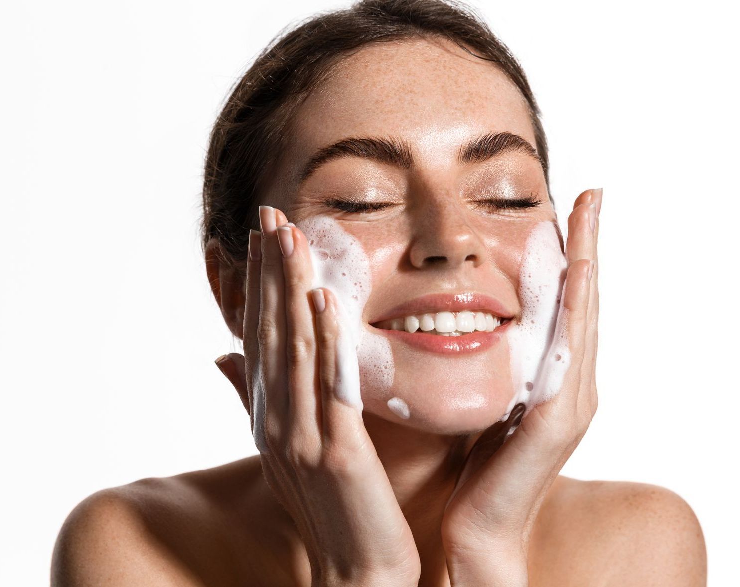 A woman is washing her face with soap and smiling.
