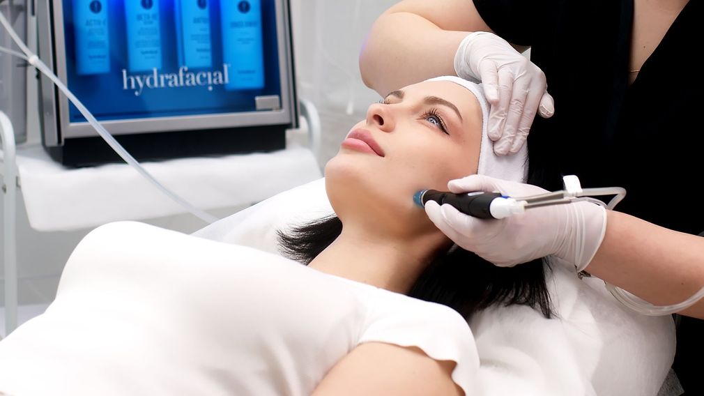 Woman receiving a facial treatment in a spa, with a skincare device applied to her cheek.