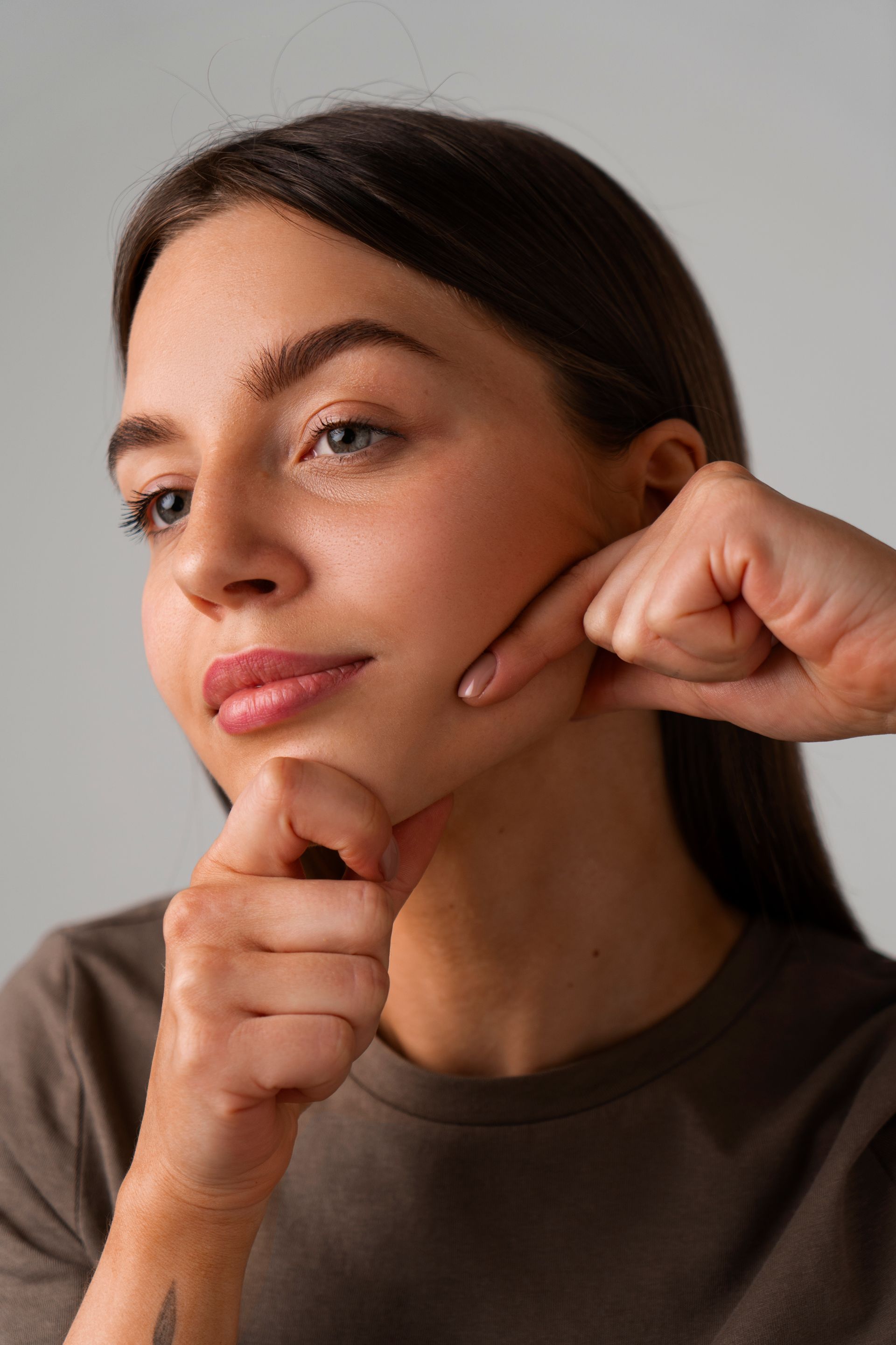 A close up of a woman's face with her hands on her chin.