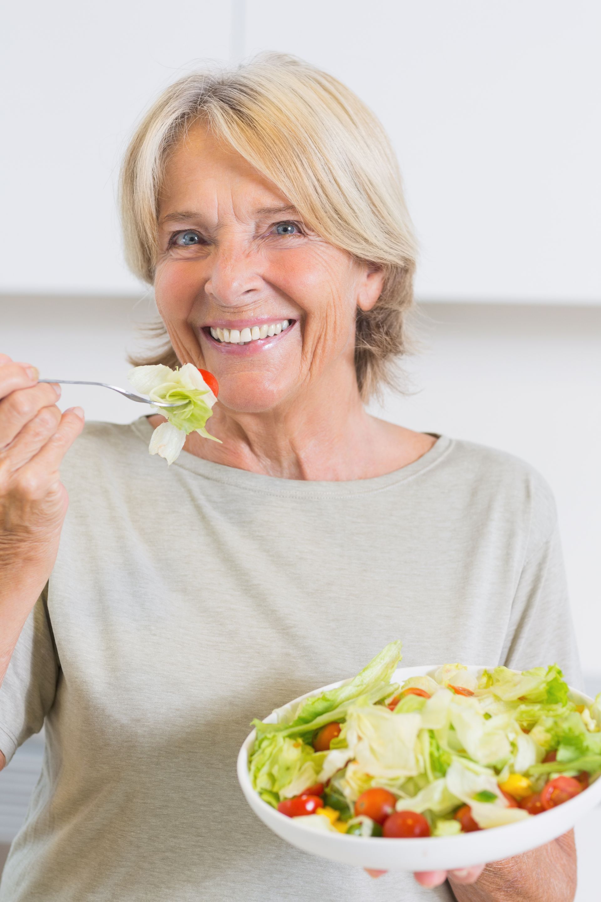 A woman is eating a salad with a fork in a kitchen.
