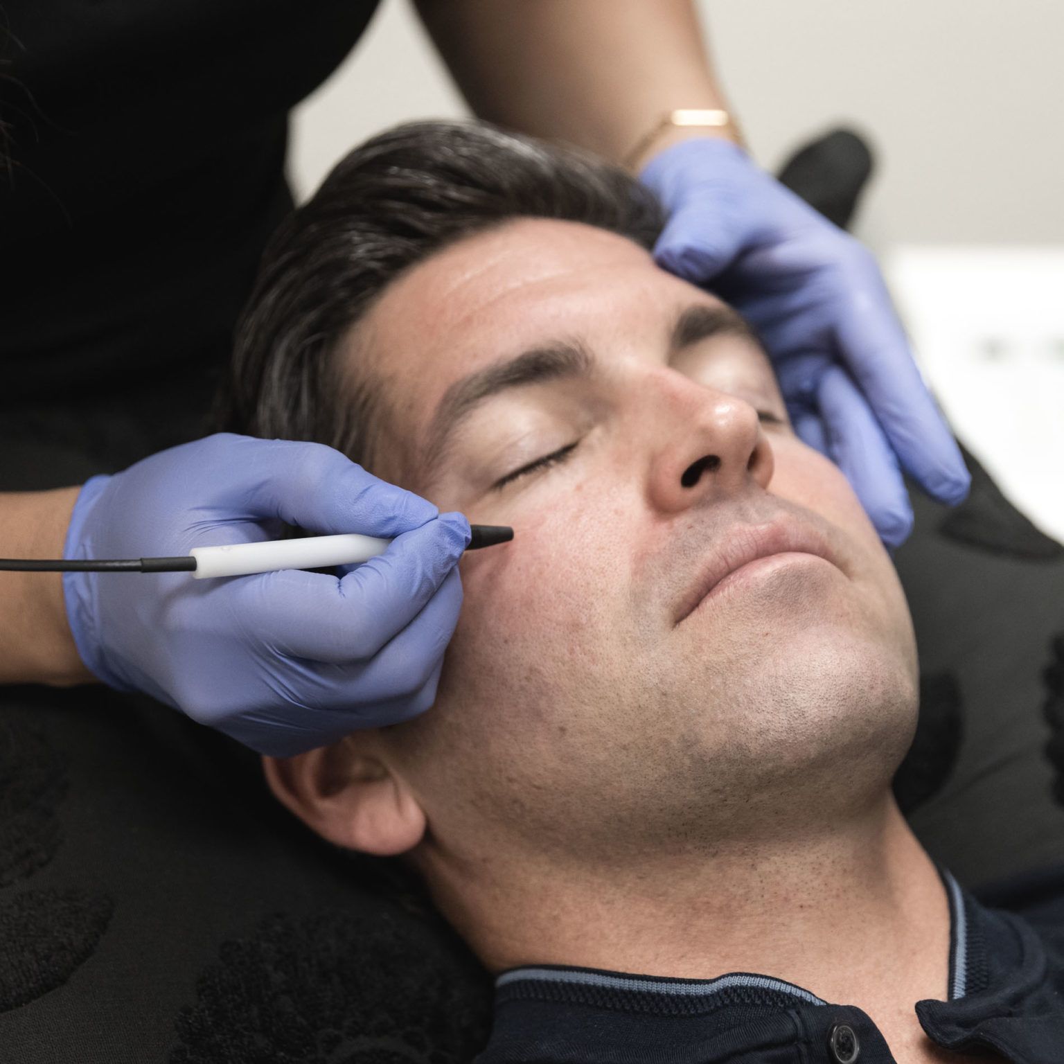 Person receiving an eyebrow treatment while lying back as gloved hands work near the eyes