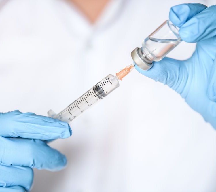 A person wearing blue gloves is holding a syringe and a bottle