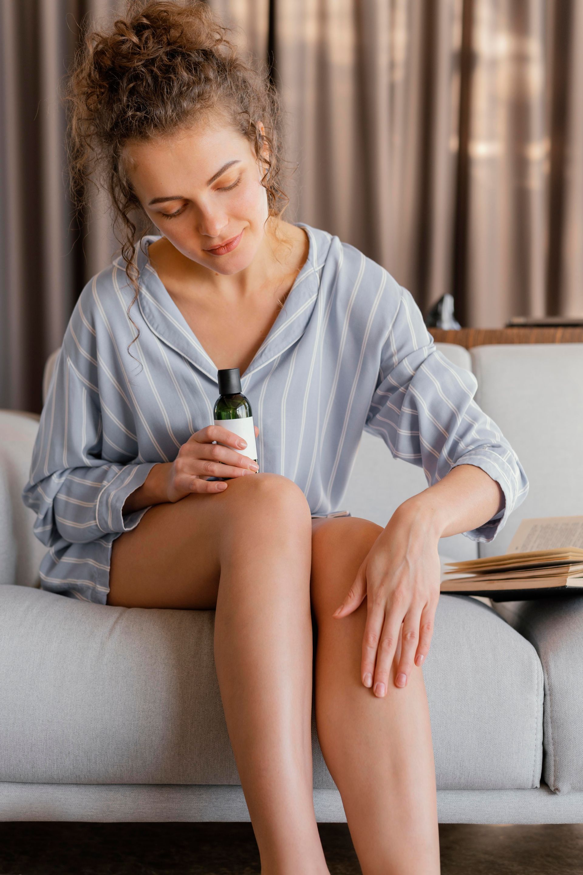 A woman is sitting on a couch applying lotion to her legs.
