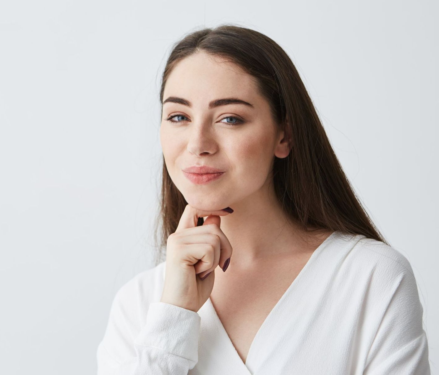 A woman in a white shirt is holding her hand to her chin.