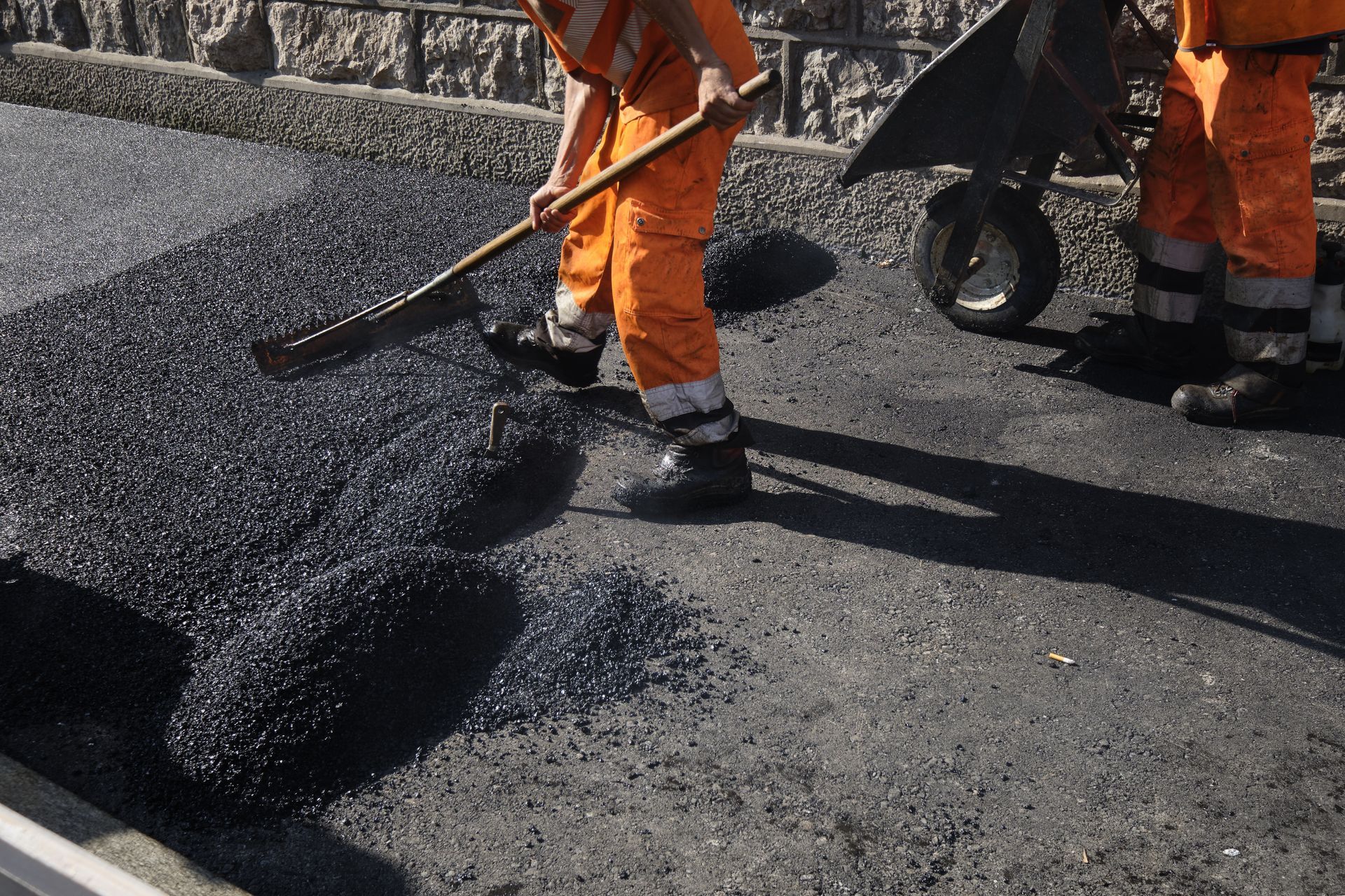 Workers are spreading asphalt with shovels and wheelbarrows during road construction.