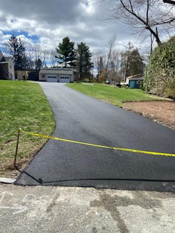 A man is using a machine to spread asphalt in a driveway.