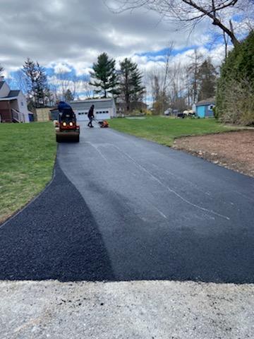 A man is walking down a paved driveway next to a house.