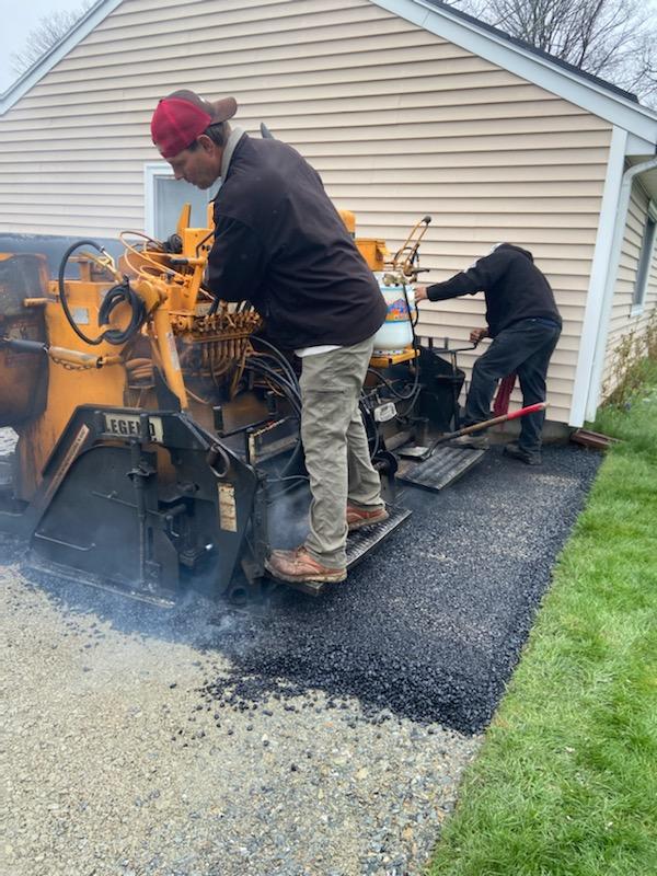 A man is using a machine to spread asphalt in a driveway.