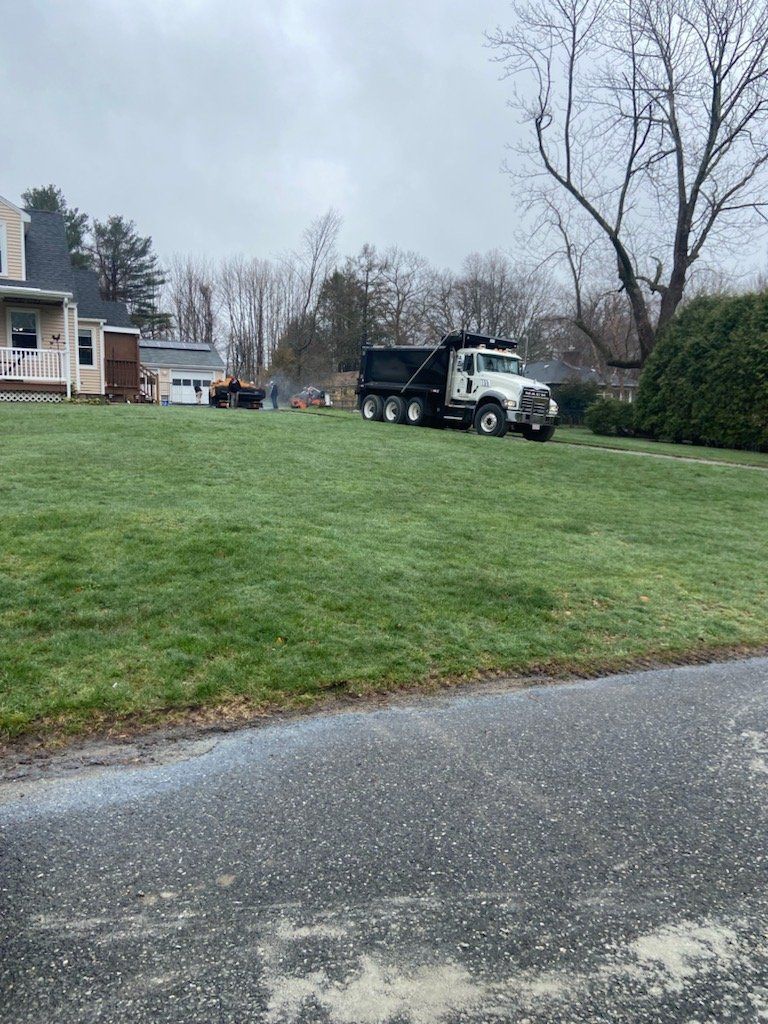 A dump truck is parked in the grass in front of a house.