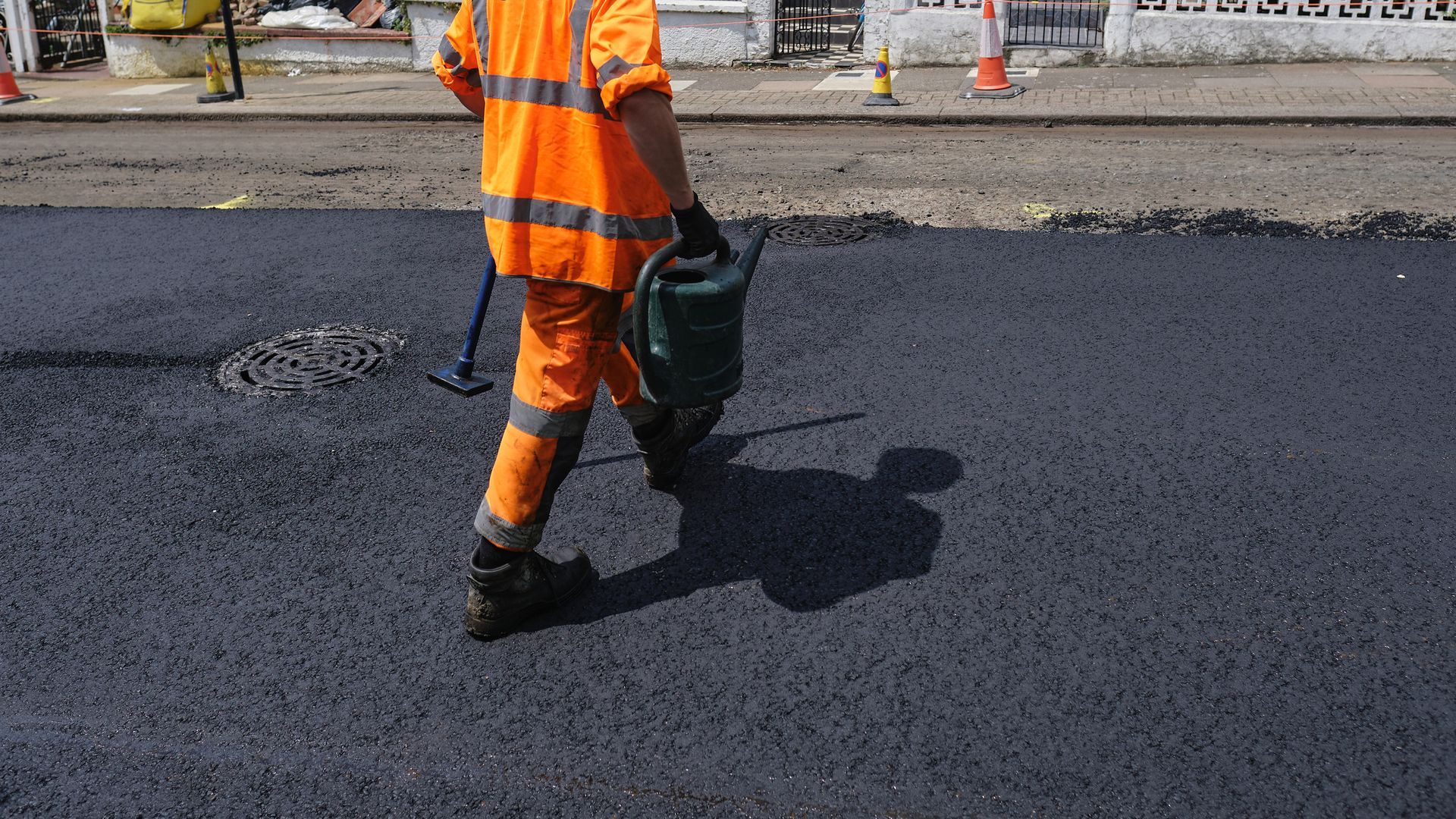Worker in orange uniform performing asphalt paving on city street with fresh black surface. Worker in orange uniform performing asphalt paving on city street with fresh black surface.