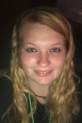 A person with shoulder-length blonde hair and a faint smile looking directly at the camera.