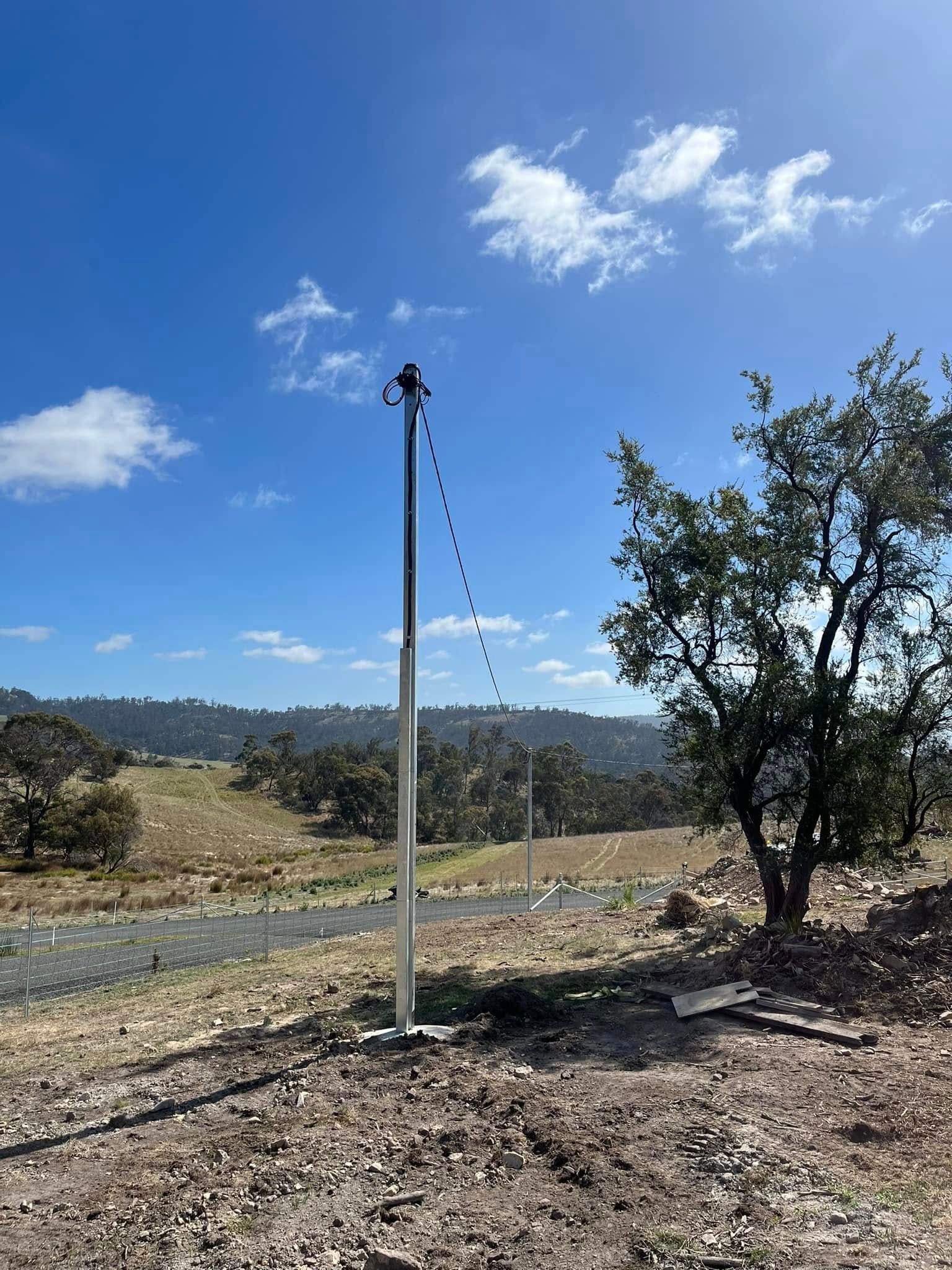 Person working in a trench, wearing shorts and boots. They are near electrical cables and a metal pole.