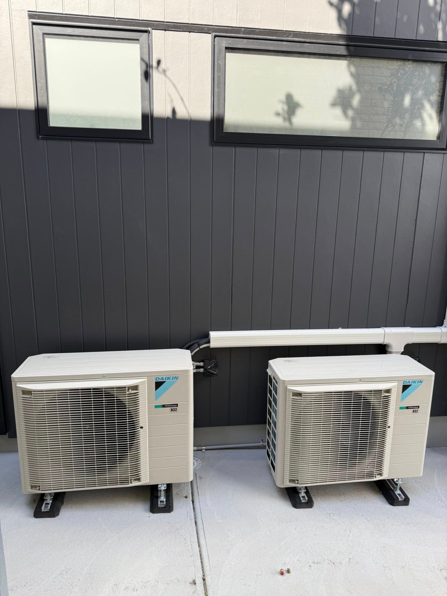 Two Daikin air conditioning units mounted on a gray wall with windows.
