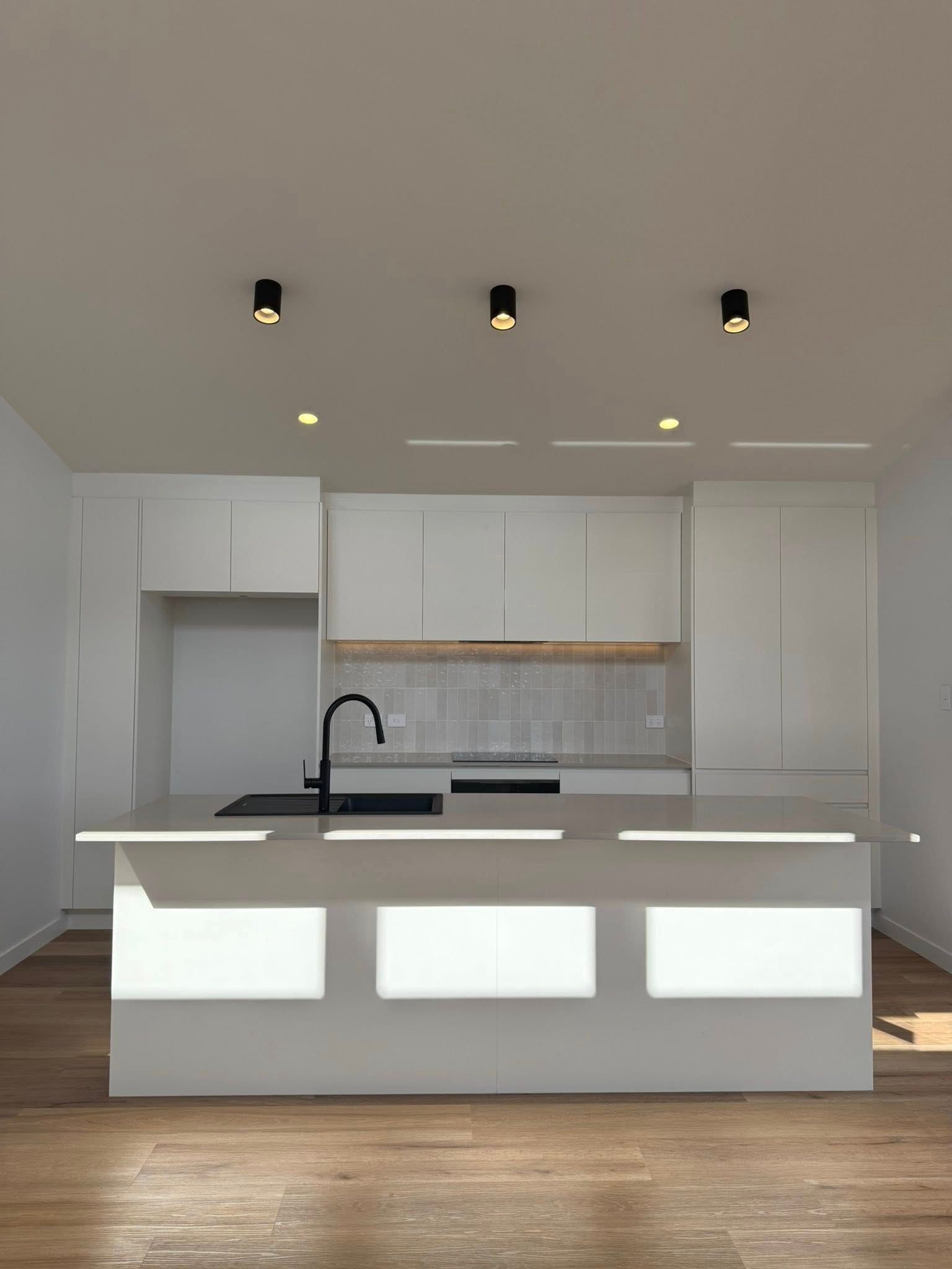 Modern white kitchen with island, black faucet, wooden floor.
