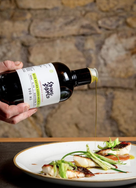 Due persone brindano con dei bicchieri di gin decorati in un bar scarsamente illuminato, festeggiando con altre persone che si intravedono sullo sfondo.