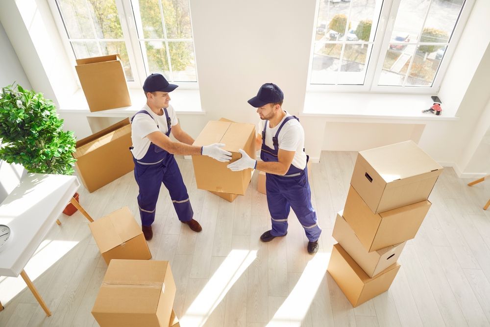 Two men are moving boxes in a room.
