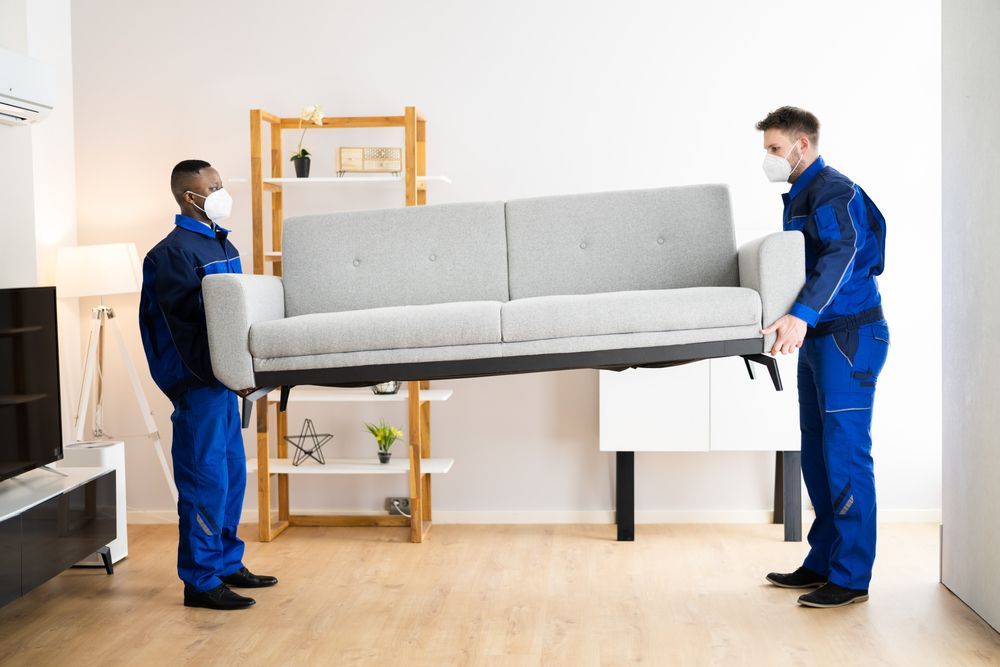 Two men are carrying a couch in a living room.