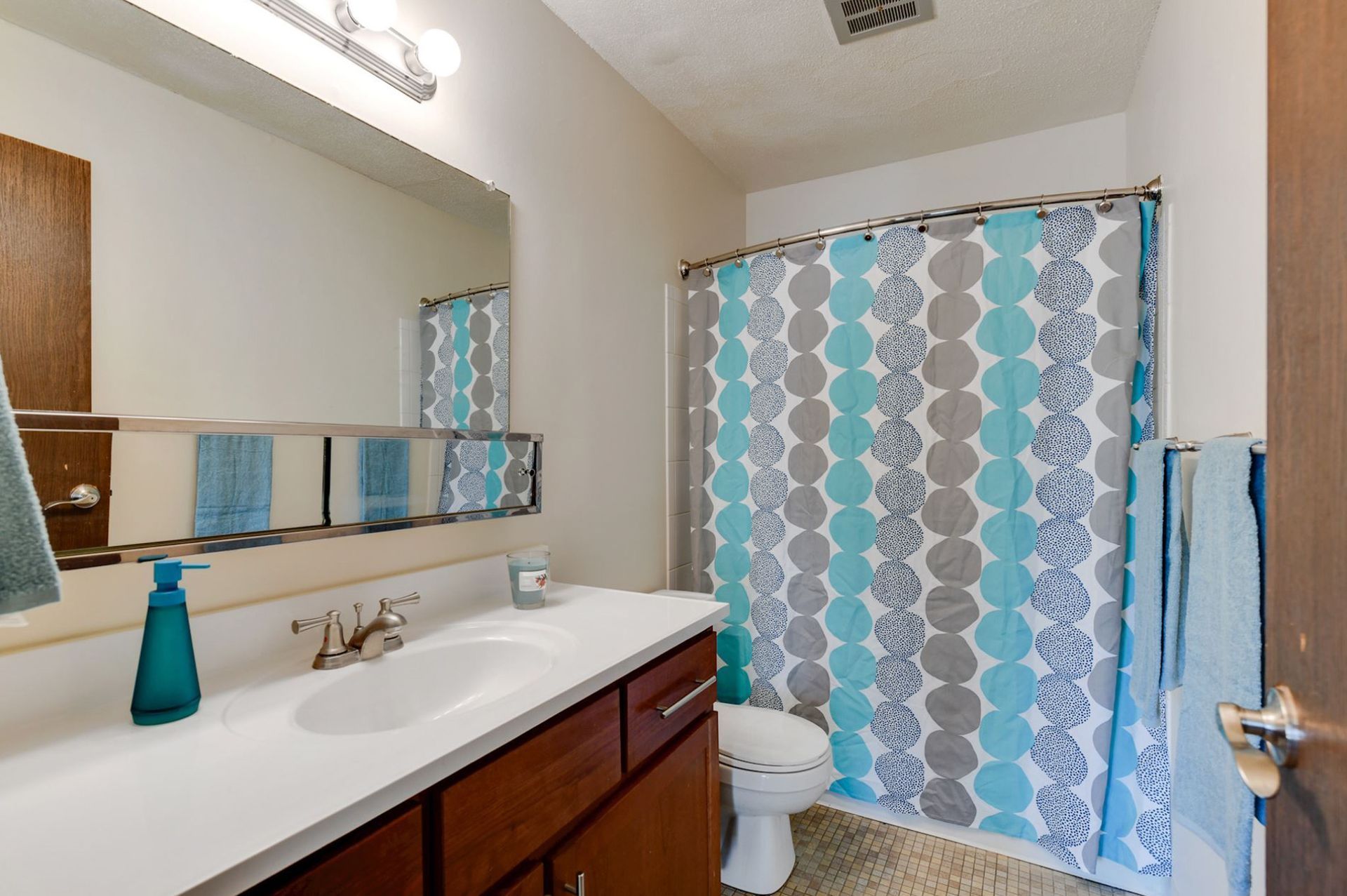 Bathroom with blue and gray patterned shower curtain, vanity with sink, and dark wood cabinets at Manor Royal in Plymouth, MN.
