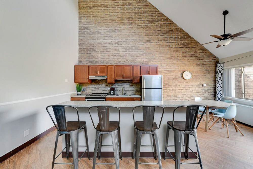 Kitchen with exposed brick wall, breakfast bar with stools, wood cabinets, stainless steel appliances, and dining area.