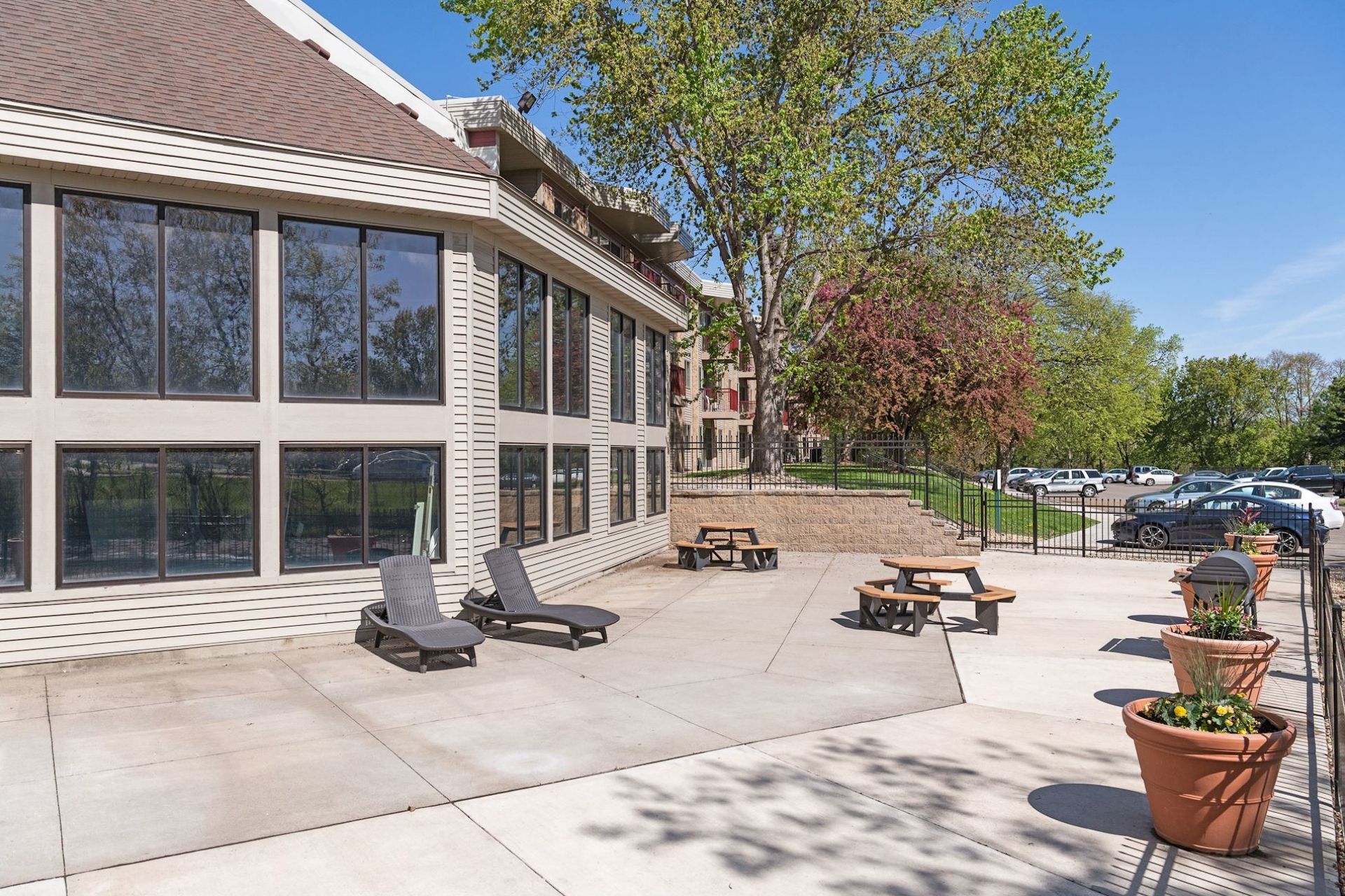 Outdoor patio with lounge chairs, picnic tables, and large windows. Brown building with trees in the background at Manor Royal in Plymouth, MN.