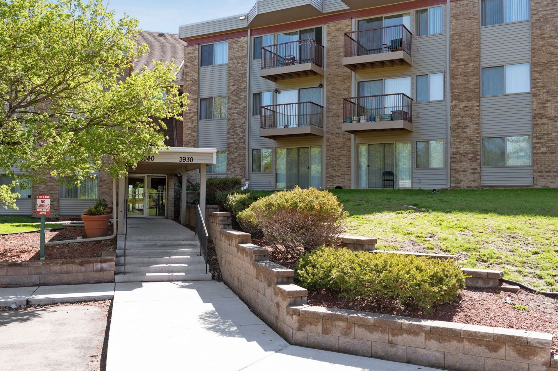 Apartment building with balconies and entrance, landscaping with stairs and bushes at Manor Royal in Plymouth, MN.