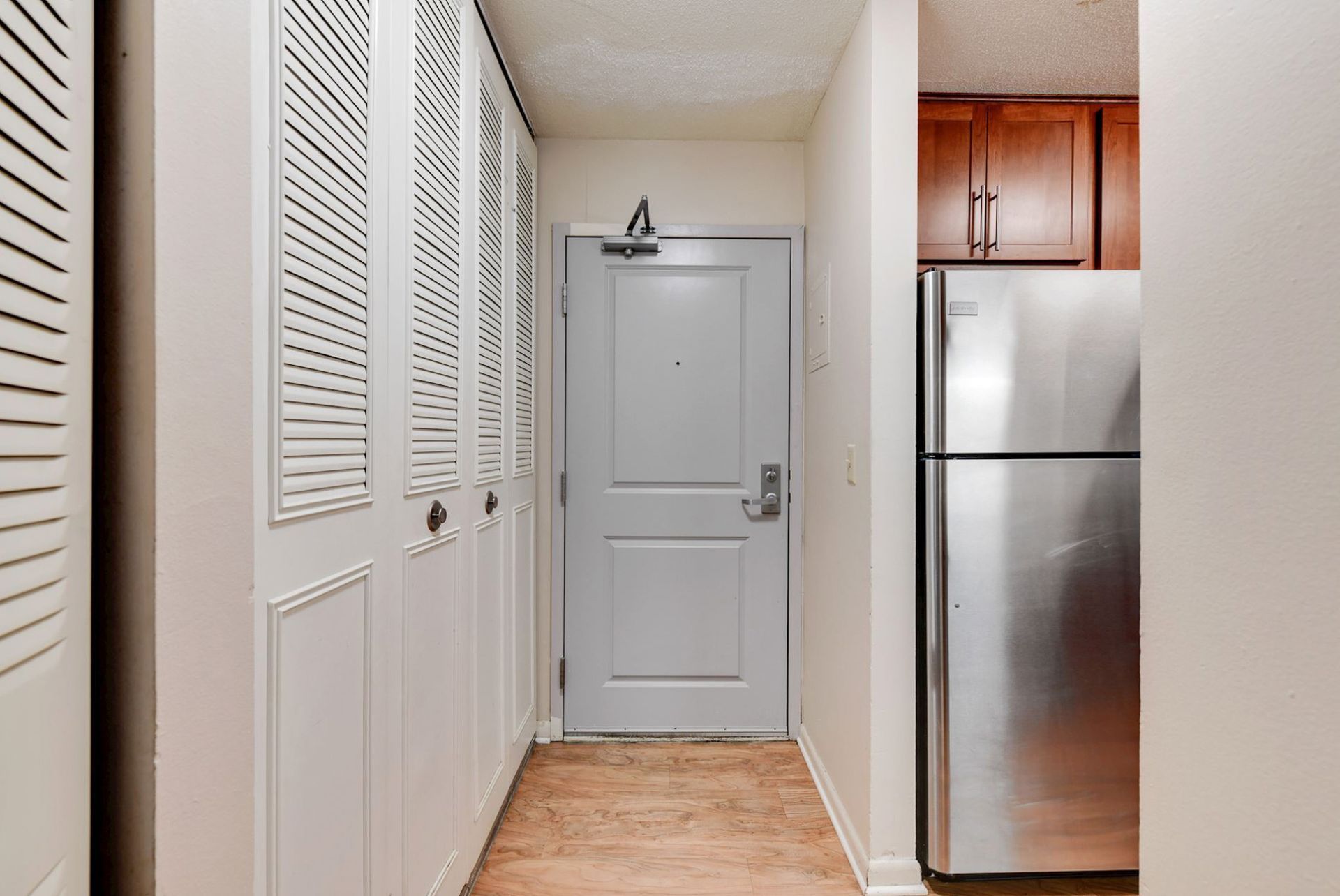 Hallway with white louvered closet doors, gray front door, and stainless steel refrigerator at Manor Royal in Plymouth, MN.