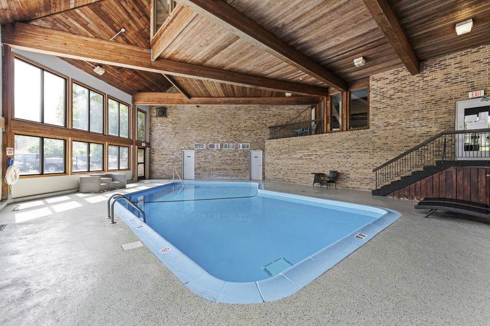 Indoor swimming pool with light blue water, brick walls, and exposed wooden beams at Manor Royal in Plymouth, MN.