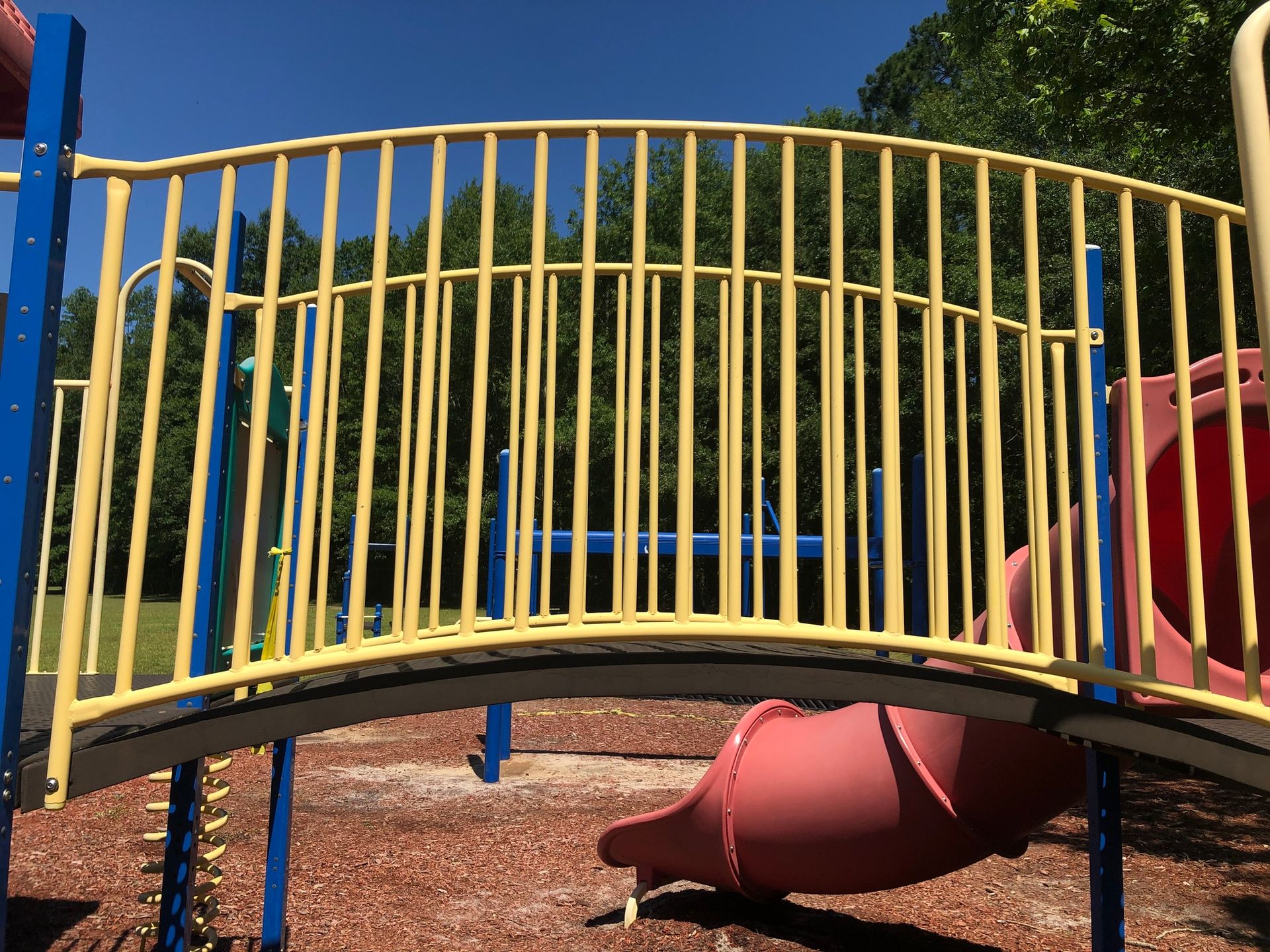 A playground with a red slide and a yellow bridge.