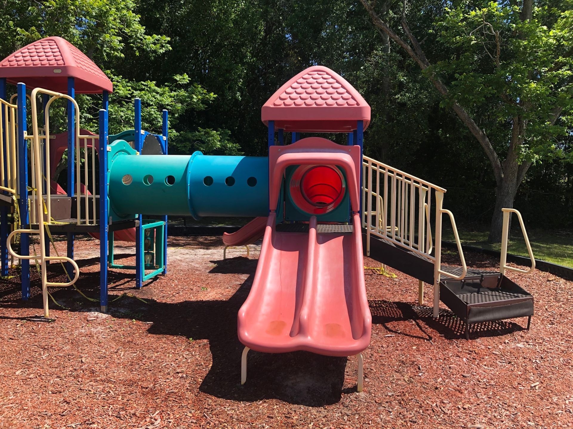 A playground with a pink slide and a blue tunnel