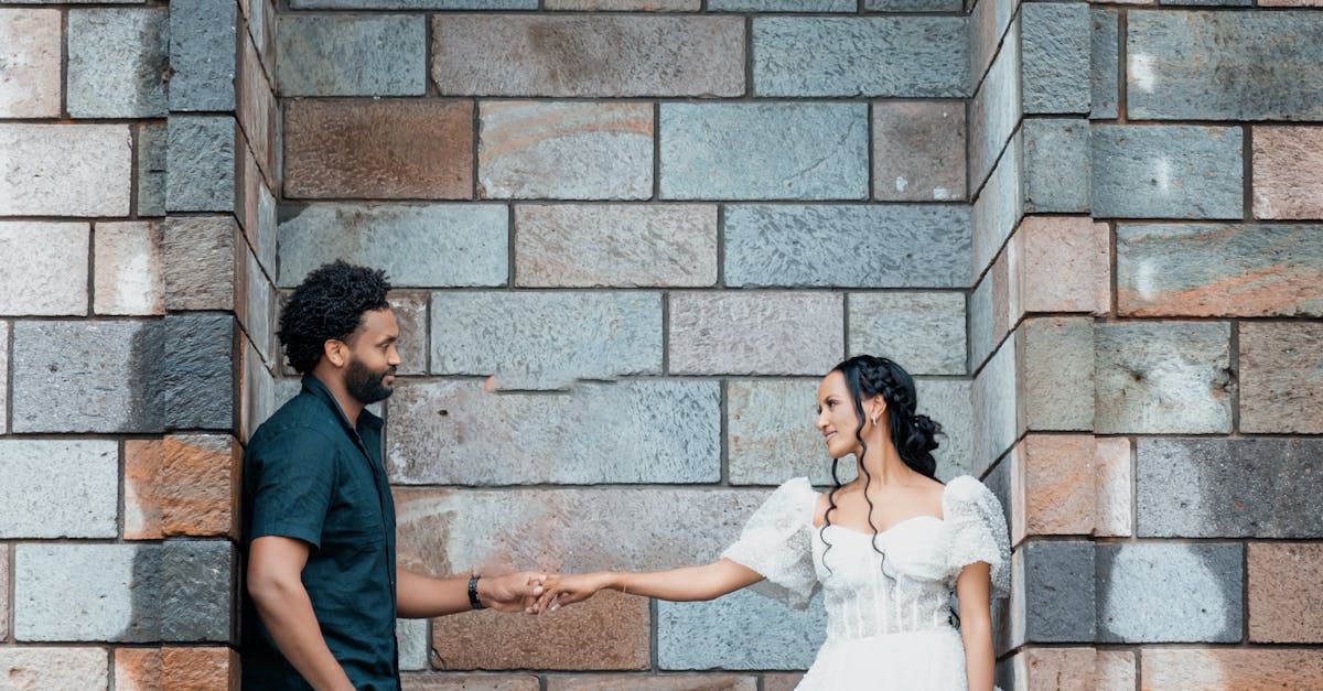 A man and a woman are holding hands in front of a brick wall.