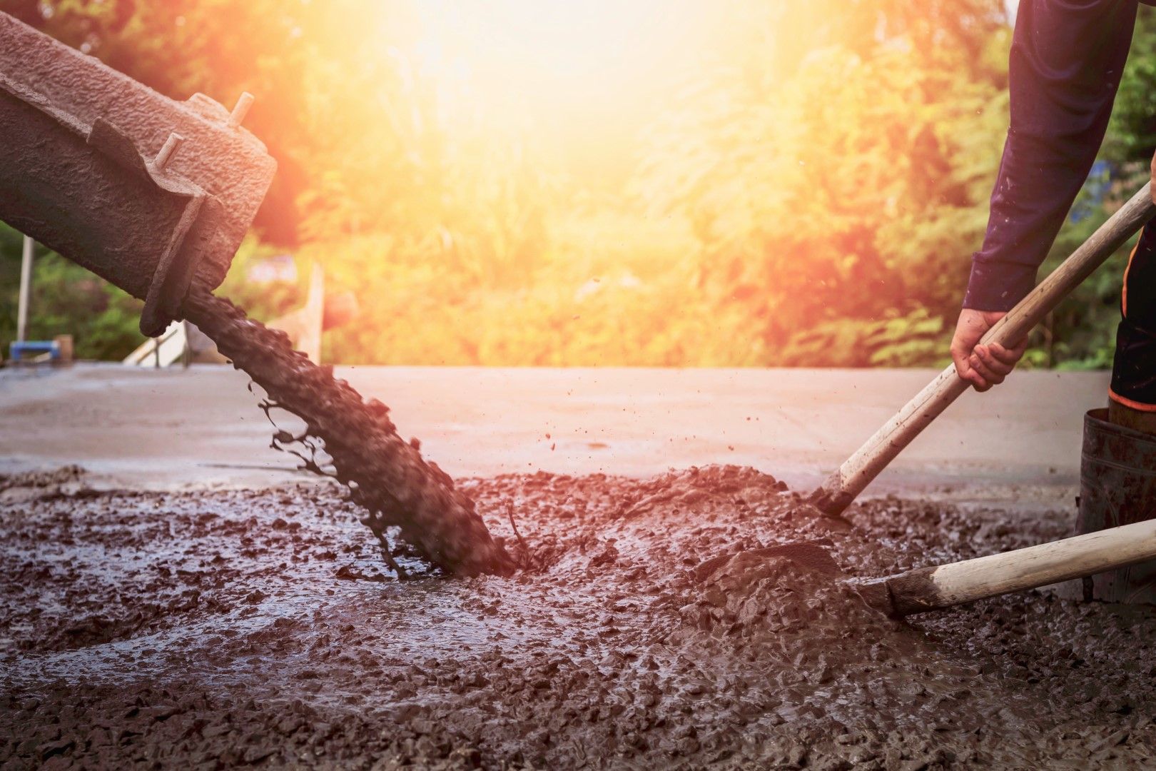A person is pouring concrete into a hole with a shovel.