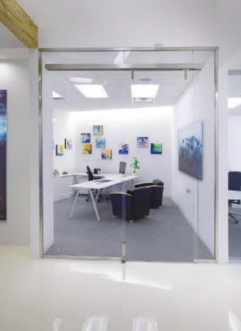 Modern office with glass walls, desk, chairs, and artwork. White and light gray color scheme.