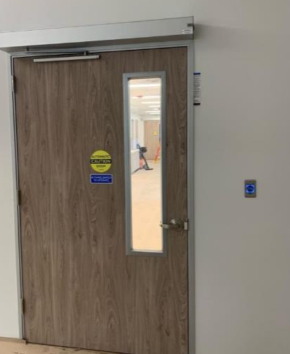 Door with window, automatic opener, push button, and signage, likely for accessibility in a building.
