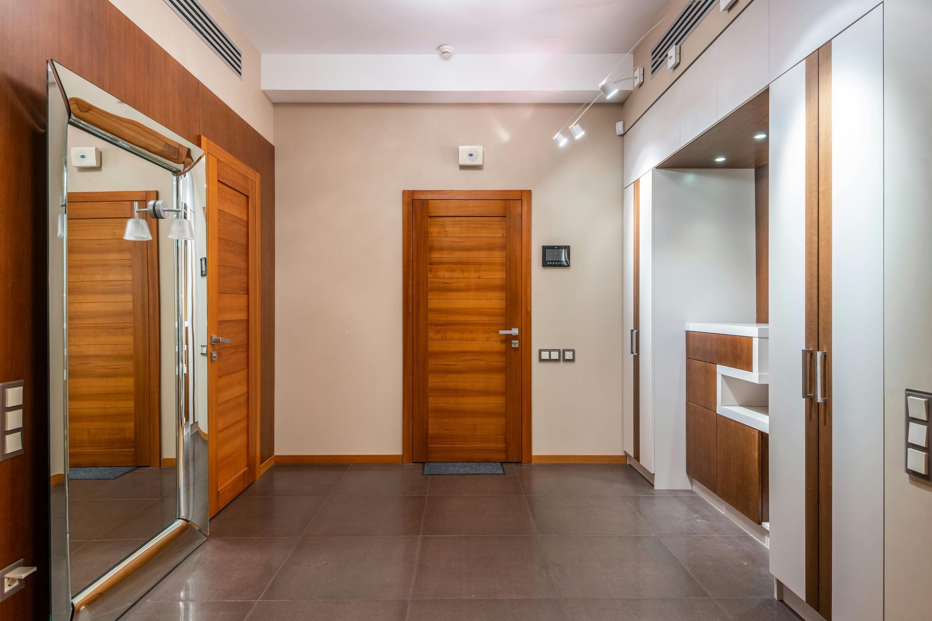 Hallway with brown doors, wooden paneling, large mirror, and tile floor.