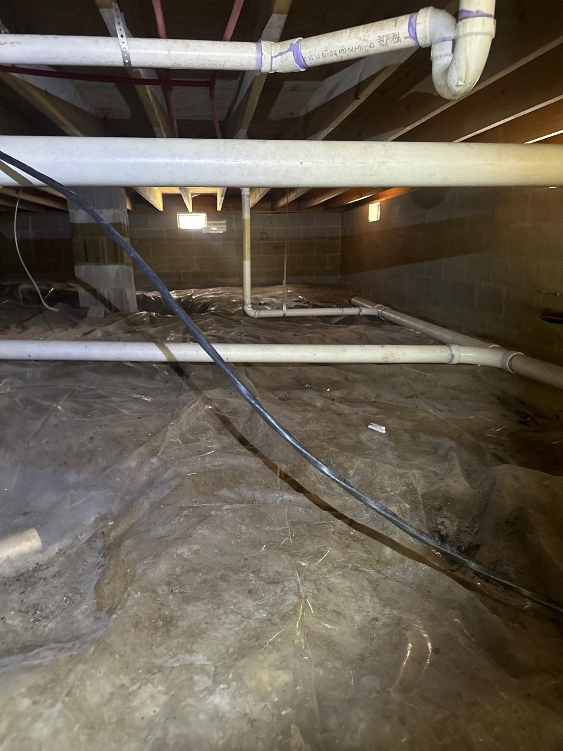 Under-house crawl space; white pipes, black cable, and exposed beams.