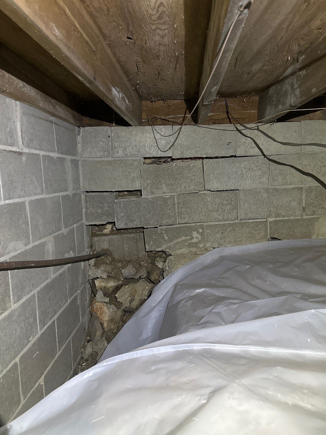 Foundation wall of cinder blocks, cracked, with exposed stonework, and plastic sheeting.
