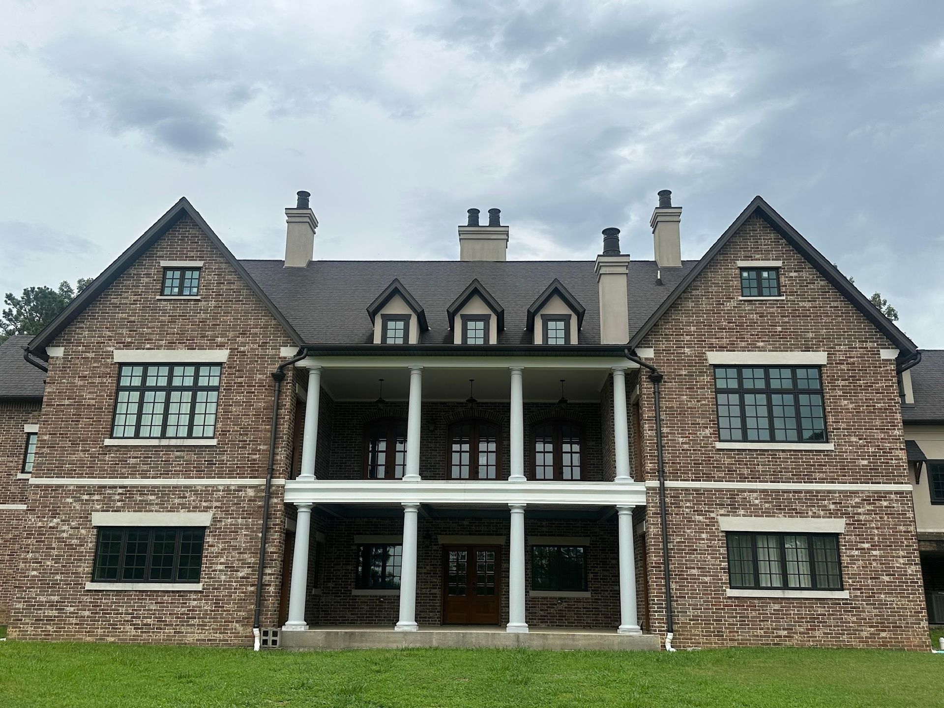 Stone mansion with pillars, dark roof, and green-framed windows, against a cloudy sky.