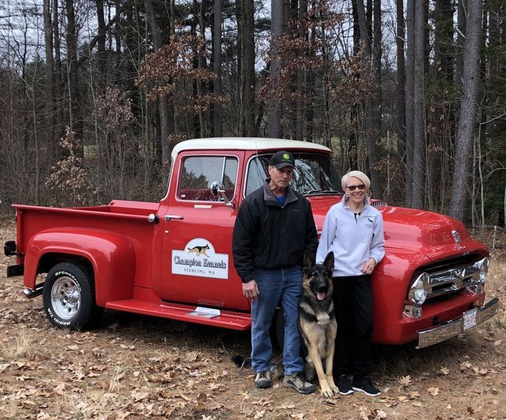 A man and a woman are standing next to a red truck.