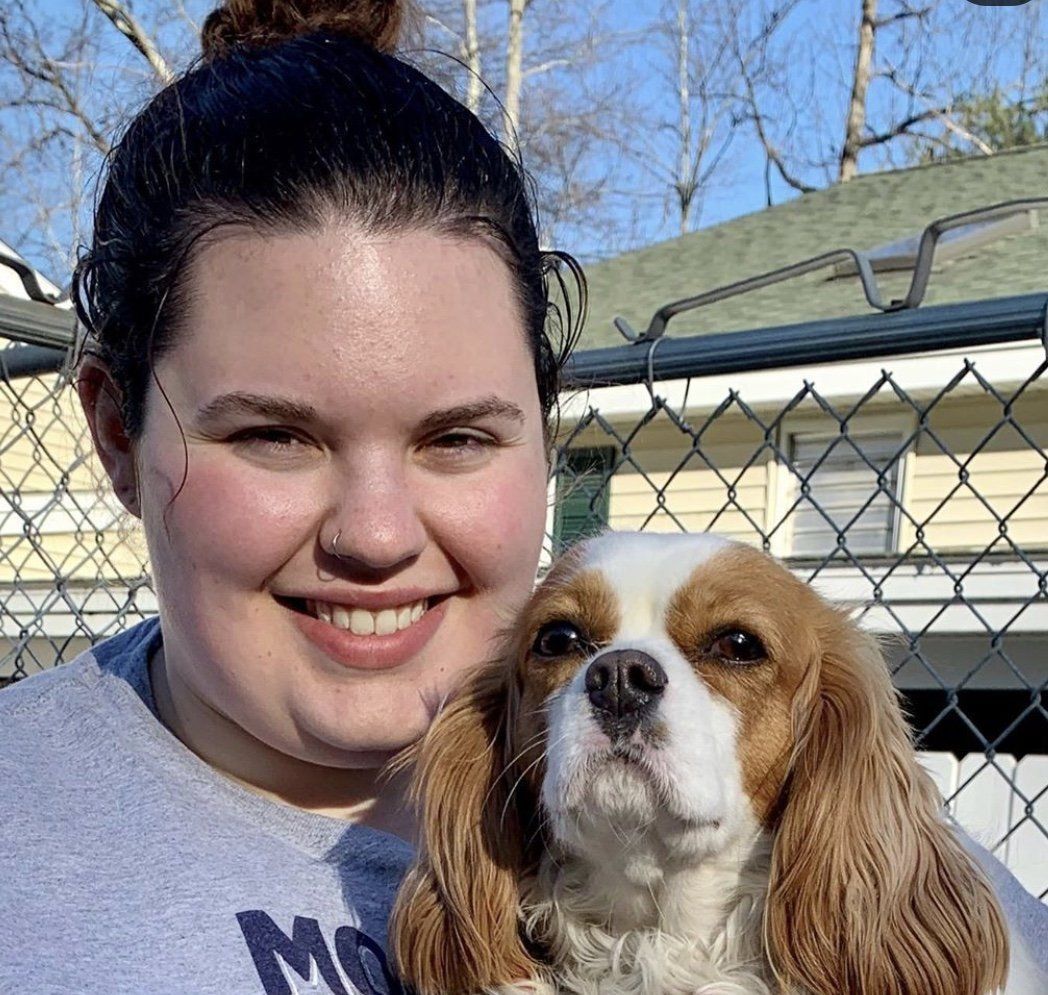 A woman is holding a brown and white dog in her arms.