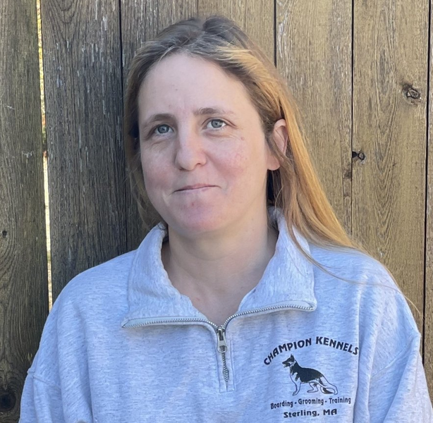A woman wearing a champion kennels sweatshirt stands in front of a wooden fence.