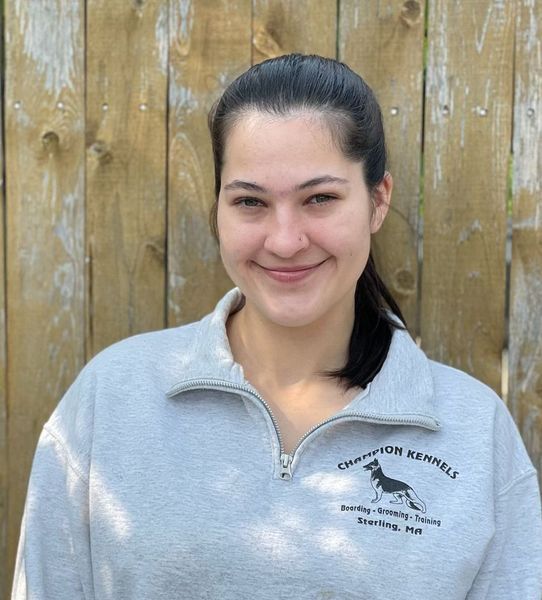 A woman wearing a champion kennels sweatshirt smiles in front of a wooden fence.