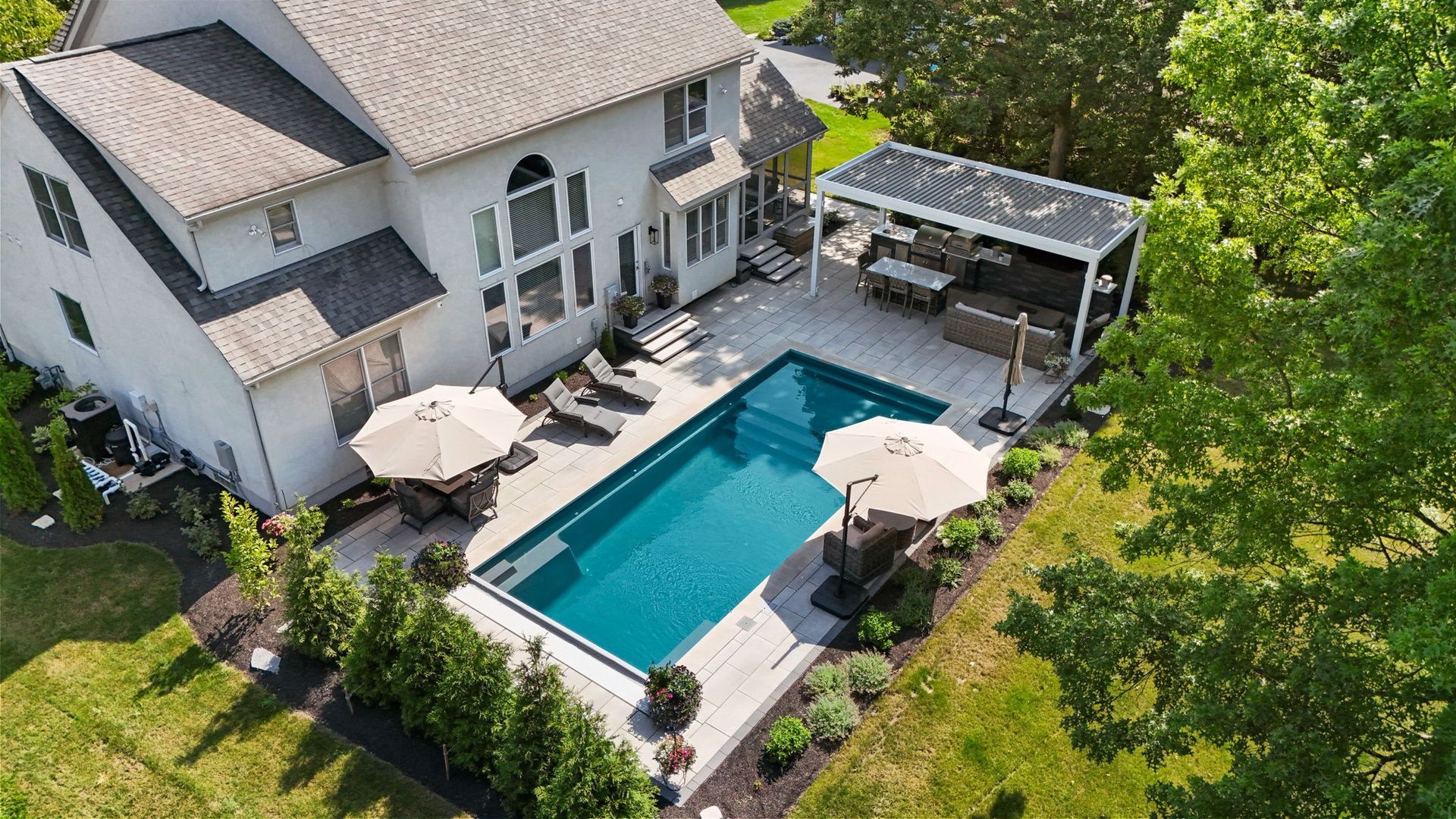 Outdoor patio with seating, a grill, and a TV, adjacent to a pool and apartment building. Features wood ceilings and blue chairs.