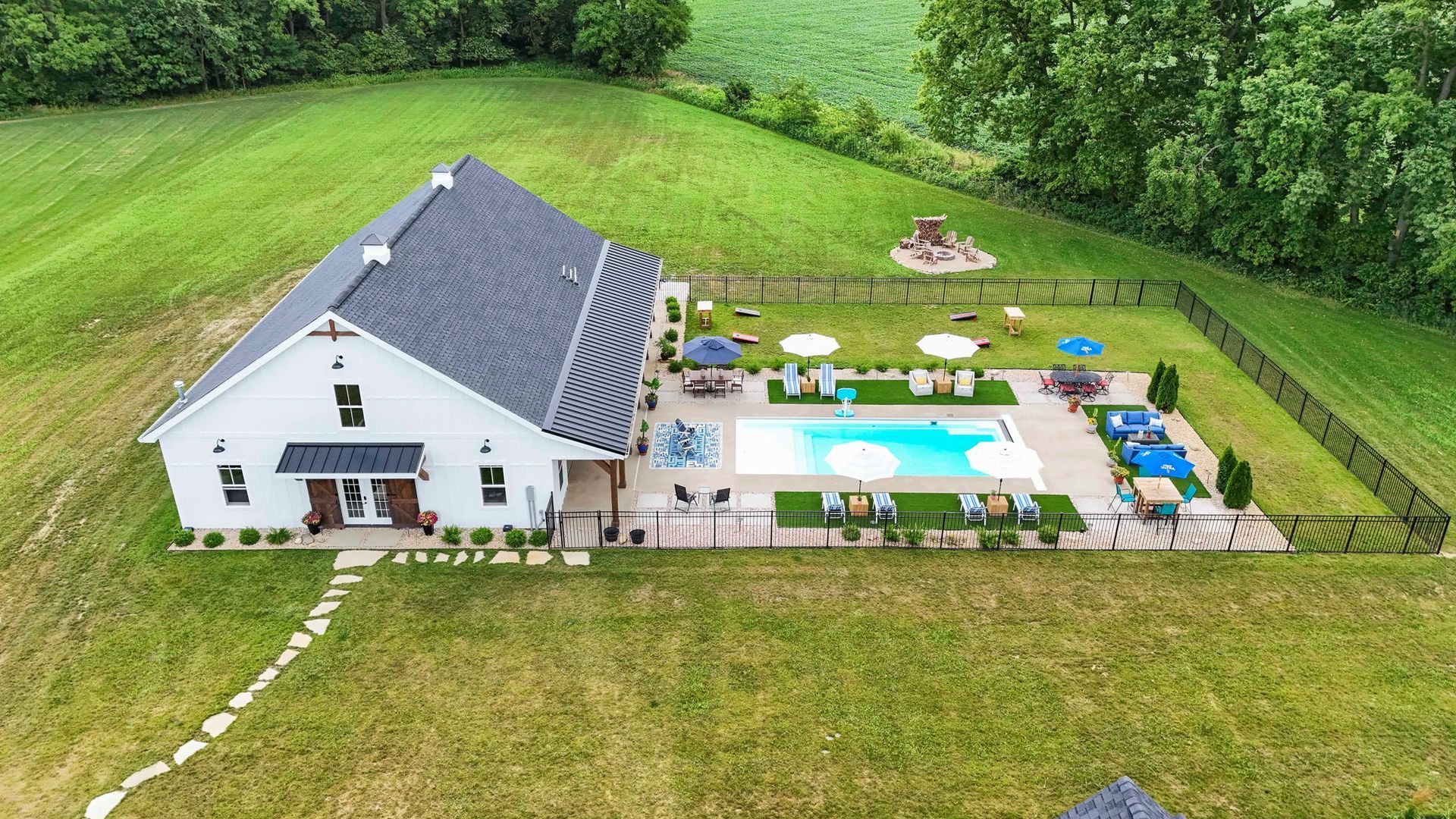 Outdoor patio with seating, a grill, and a TV, adjacent to a pool and apartment building. Features wood ceilings and blue chairs.