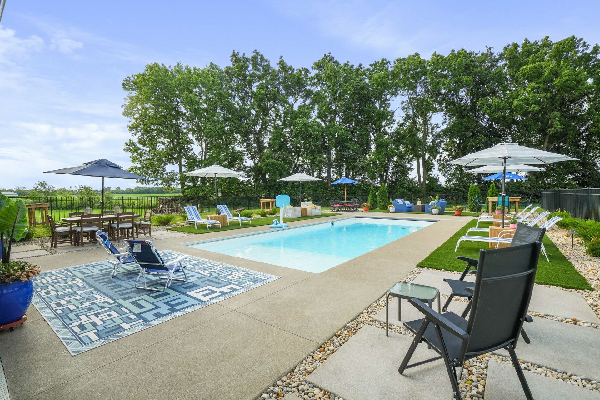 Overhead view of a turquoise swimming pool surrounded by patio seating, artificial grass, and modern buildings.