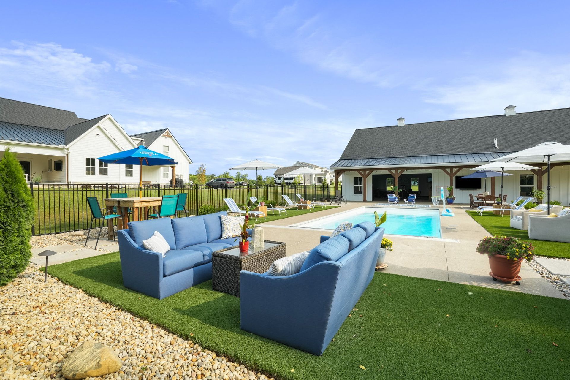 Pool area with lounge chairs, a modern building, and trees on a sunny day. A large white planter sits in the foreground.