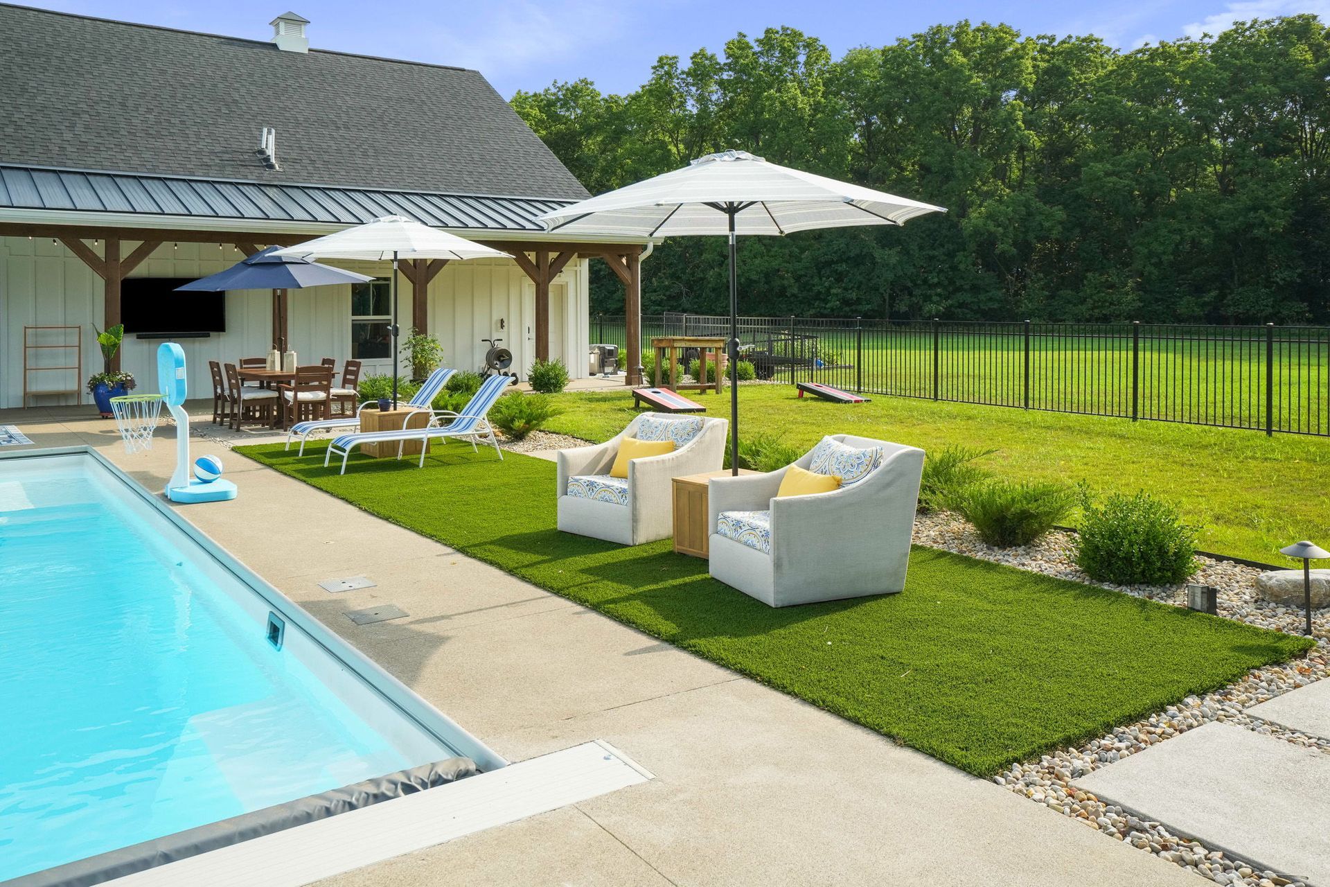 A rectangular pool in a modern apartment complex, with lounge chairs, and buildings in the background under a sunny sky.